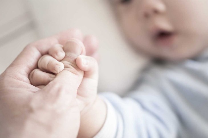 Little newborn baby holding parent\'s one hand, close-up macro shot. Focus on foreground. The touching and lovely moment. Concept of support, hope, love, bonding and care, hold on...