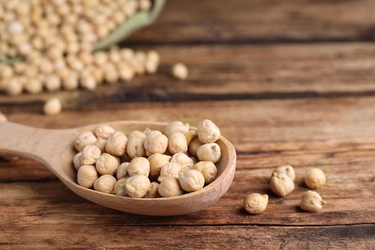 Spoon with chickpeas on wooden table, closeup. Space for text