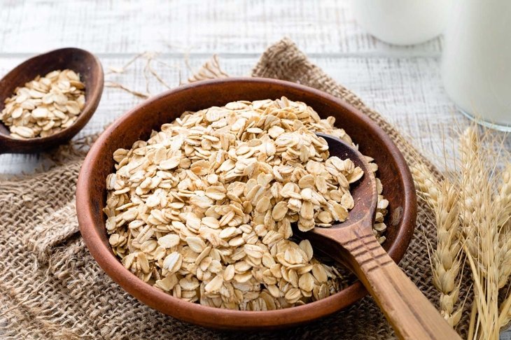 Rolled oats or oat flakes in bowl with wooden spoons, golden wheat ears and bottle of milk on background. Healthy lifestyle, healthy eating concept