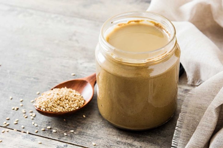 Tahini and sesame seeds on wooden table.