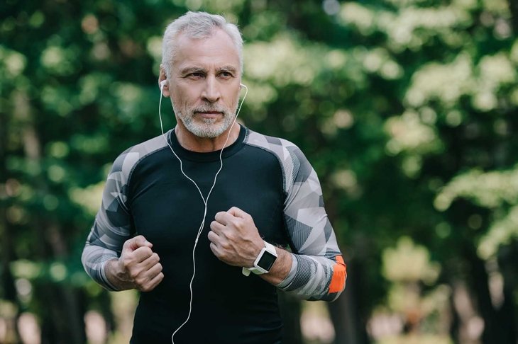 handsome mature sportsman listening music in earphones while running in park