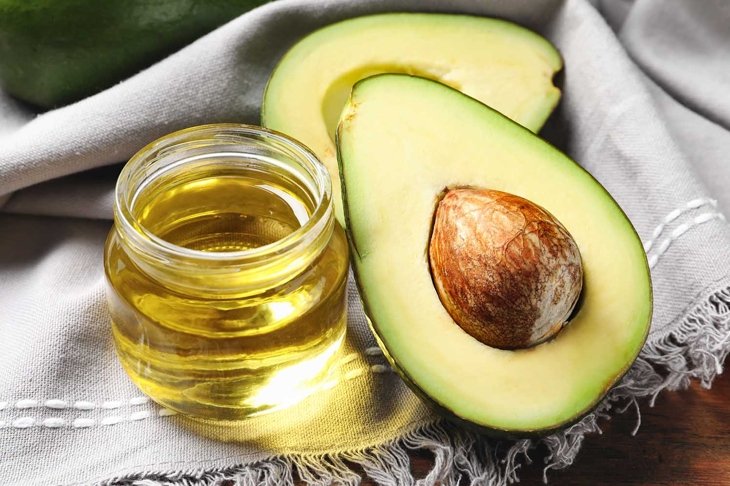 Jar with oil and ripe fresh avocado on table, closeup