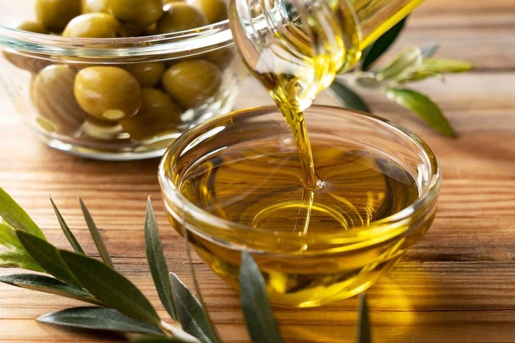 The moment olive oil is poured into a glass bowl set against a wooden background