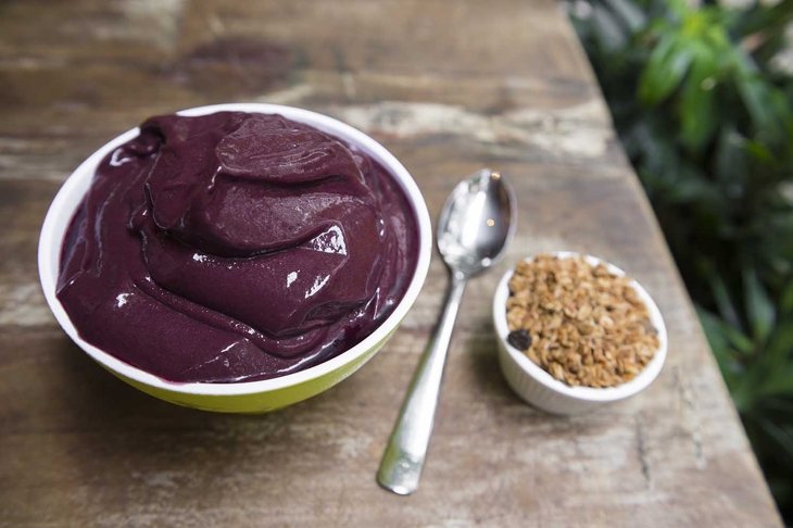 Bowl of fresh Brazilian acai (açaí) garnished with granola on a rustic wood table in Rio de Janeiro, Brazil