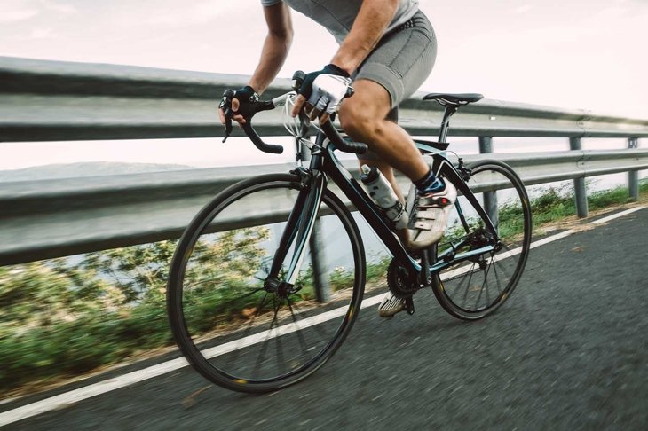 Detail of a road bike with a cyclist pedaling on a road.