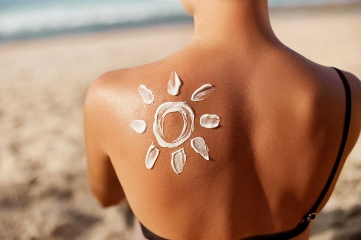 Woman Applying Sun Cream on Tanned Shoulder In Form Of The Sun. Sun Protection.Sun Cream. Skin and Body Care. Girl Using Sunscreen to Skin. Female Holding Suntan Lotion and Moisturizing Sunblock.