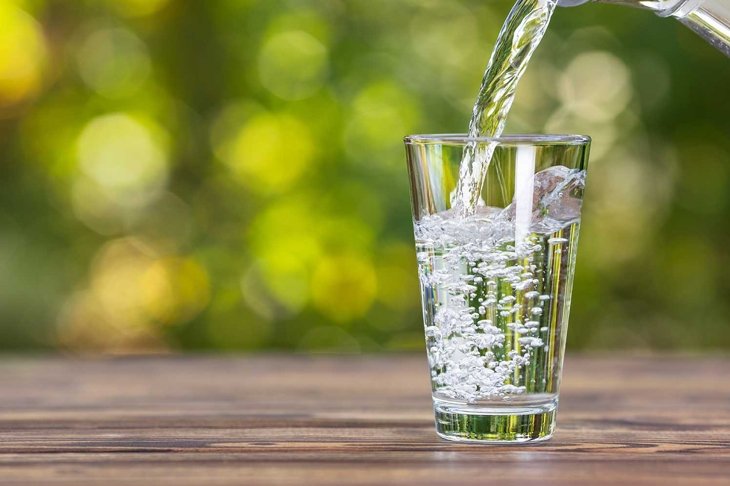 water from jug pouring into glass on wooden table outdoors